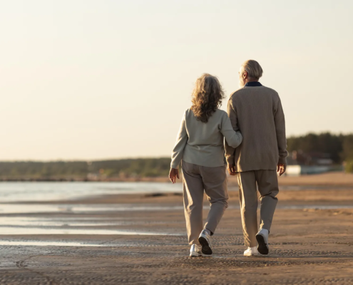 Un couple senior se promène sur la plage, symbolisant la sérénité et la planification successorale sereine.