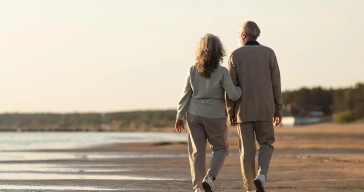 Un couple senior se promène sur la plage, symbolisant la sérénité et la planification successorale sereine.