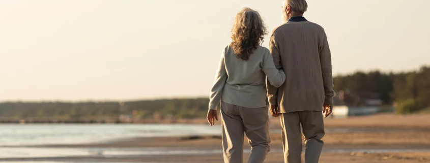 Un couple senior se promène sur la plage, symbolisant la sérénité et la planification successorale sereine.