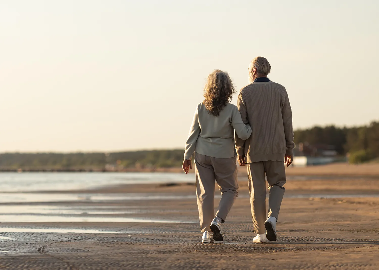 Un couple senior se promène sur la plage, symbolisant la sérénité et la planification successorale sereine.